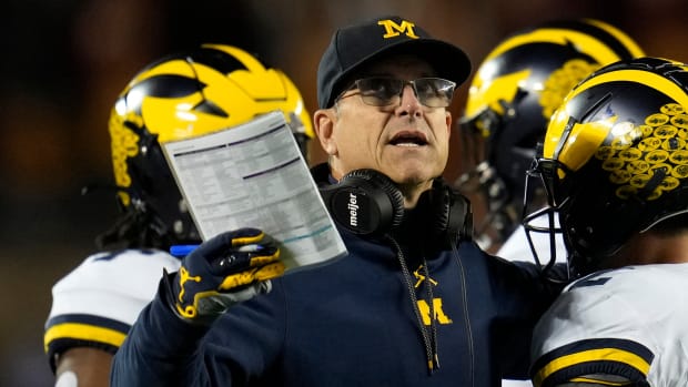 Michigan coach Jim Harbaugh motions while standing on the sideline among his players.